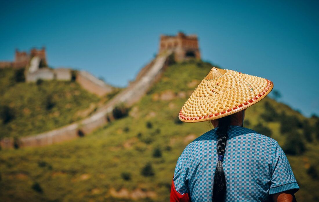 Mujer con sombrero y vestimenta tradicional frente a la Gran Muralla China, parte del tour organizado por Orient Tours.