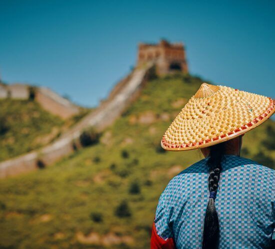 Mujer con sombrero y vestimenta tradicional frente a la Gran Muralla China, parte del tour organizado por Orient Tours.